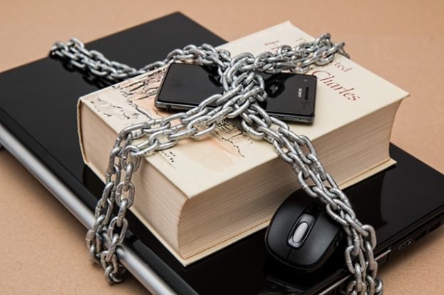 Laptop, phone, mouse and book with chains wrapped around