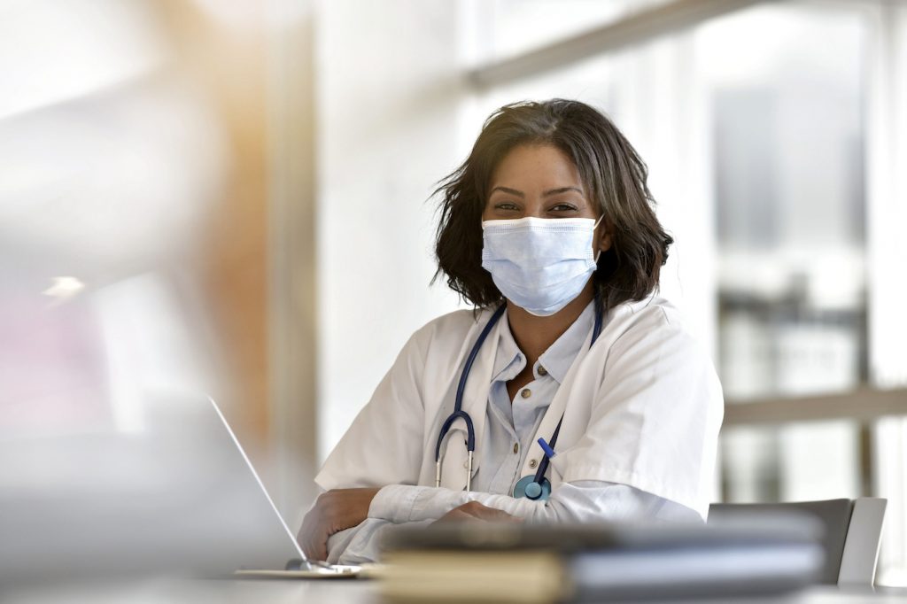 Woman doctor working in office with laptop computer; wearing face mask